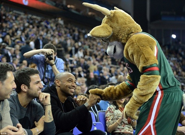 Milwaukee Bucks mascot Bango shakes hands with Arsenal legend Thierry Henry from courtside at the O2 Arena