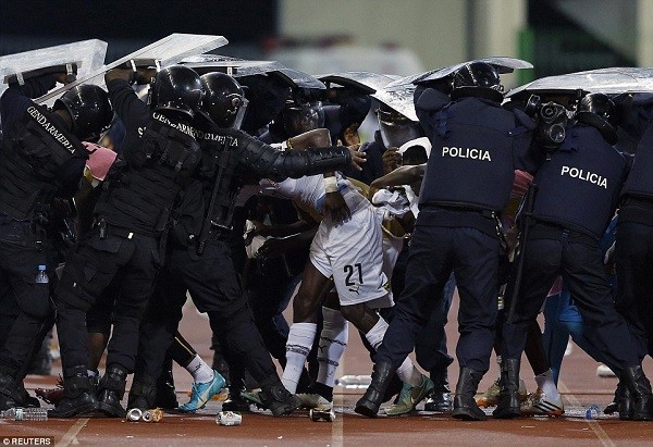 Ghana players are shielded by riot police after being pelted by missiles by an infuriated home crowd as they left the pitch for half-time