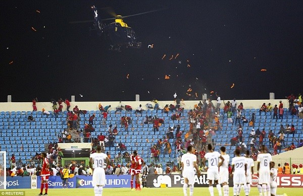 Players wait on the pitch as a helicopter tries to control an agitated crowd in Malabo by flying low over the stands and kicking up debris