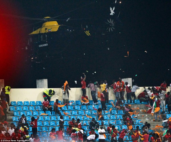 Spectators dive for cover in the stands as the helicopter passing overhead sends debris swirling up into the air