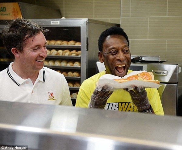 A beaming Pele prepares to take a bite from a footlong as former Liverpool striker Robbie Fowler looks on