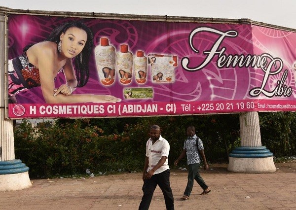 Two men walk under a giant advertisement for skin-lightening products in Abidjan